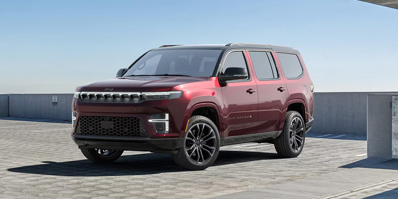 A burgundy Jeep SUV parked on a paved surface with a clear sky in the background.